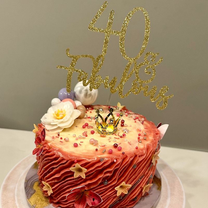 Pink birthday cake with a gold topper and sugar flowers